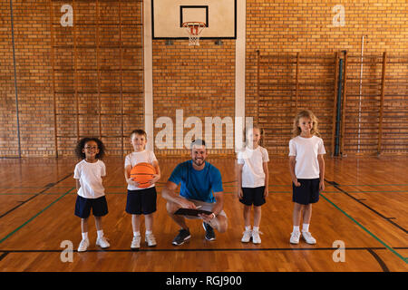Happy basketball coach and schoolkids looking at camera at basketball court Stock Photo