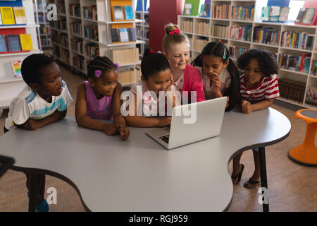 Side view of schoolkids studying together on laptop at table in school library Stock Photo
