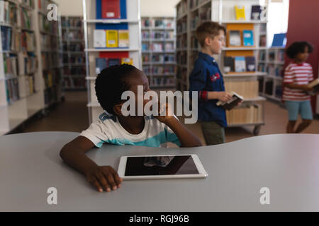 Thoughtful schoolboy with hand on chin looking away sitting at table in school library Stock Photo
