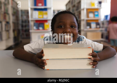 Happy schoolboy leaning his face on books and looking at camera on table Stock Photo