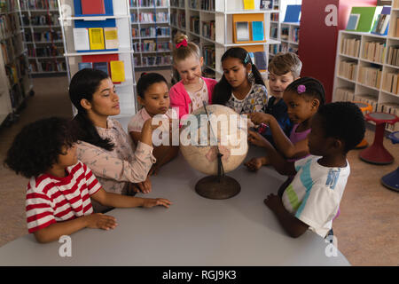 Front view of female teacher teaching the kids about the globe at table in school library Stock Photo