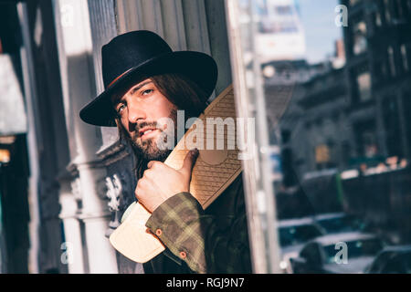 USA, New York City, portrait of bearded man with skateboard wearing black hat Stock Photo