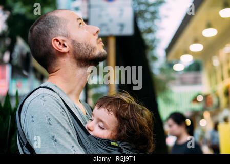 China, Hong Kong, father travelling with little girl sleeping in a baby carrier