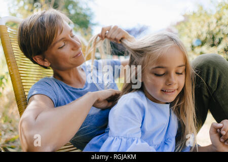 Mother braiding daughter's hair in garden Stock Photo