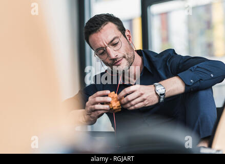 Mature man sitting in office assembling wooden cube puzzle Stock Photo
