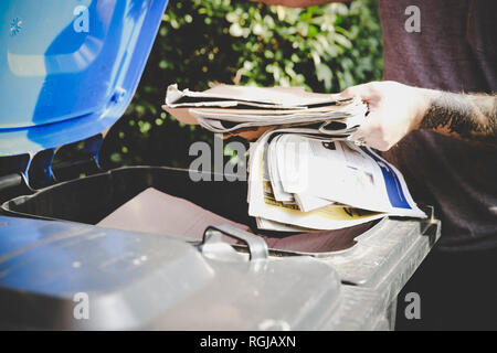 Tattooed man recycling waste paper in paper bank, partial view Stock Photo