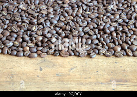 Lot of scattered roasted coffee beans on an old wooden table front view Stock Photo