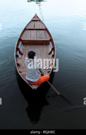 A lone female rows her wooden row boat in calm smooth water from darkness to white. Stock Photo