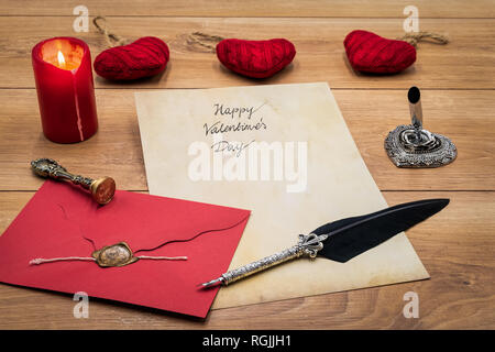 Vintage classic Valentine’s Day love cad hand written vintage paper red envelope with wax seal cuddle hart candle silver quill stand on rustic oak Stock Photo