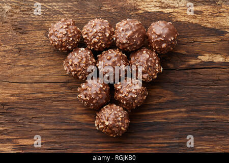 Chocolate truffle candies with hazelnuts shaped in triangle on wooden background, top view Stock Photo