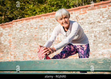 Smiling senior woman stretching on a bench