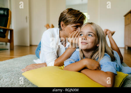 Mother and daughter lying on the floor at home whispering Stock Photo