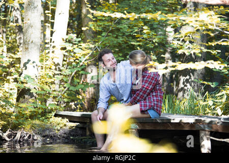 Young couple sitting on a bridge in forest with feet in water Stock Photo