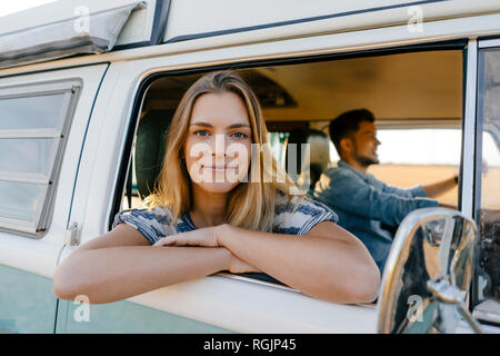 Portrait of smiling woman leaning out of window of a camper van with man driving Stock Photo