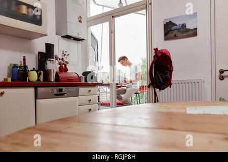 Young man sitting on balcony at home reading map Stock Photo