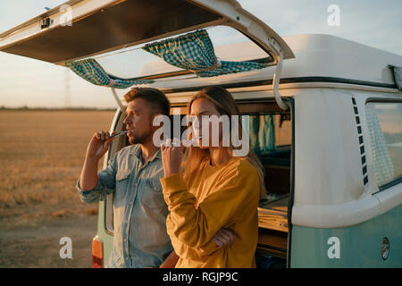 Couple brushing teeth at camper van in rural landscape at sunset Stock Photo