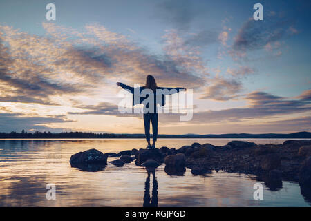 Young woman standing at lake Inari, with arms outstretched, Finland Stock Photo
