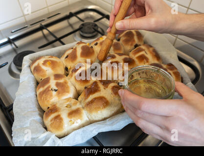 Glazing freshly baked hot cross buns Stock Photo