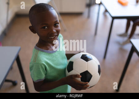 Smiling schoolboy holding football in classroom Stock Photo