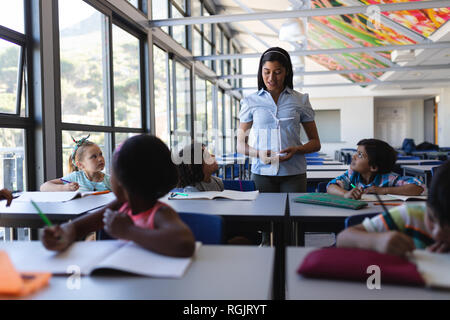 Front view of female teacher teaching student at desk in classroom of elementary school Stock Photo