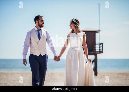 Happy bridal couple walking hand in hand on the beach Stock Photo