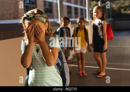 School friends bullying a crying girl in hallway of elementary school Stock Photo
