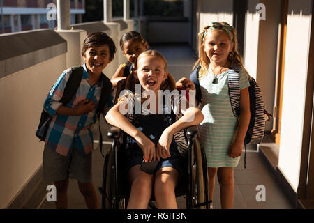 Front view of disable schoolgirl with classmates looking at camera in hallway of elementary school Stock Photo