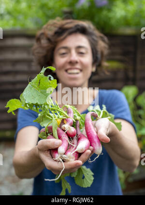 Happy veggie grower holding out freshly picked radish bunch from garden allotment Stock Photo