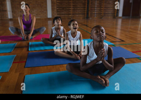 Female yoga teacher and schoolkids doing yoga and meditating on a yoga mat in school Stock Photo