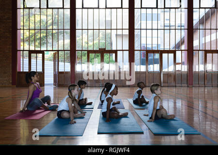 Side view of female yoga teacher and schoolkids doing yoga and meditating on a yoga mat in school Stock Photo