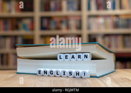 Dice in a book form the words 'learn English'. The book is lying on a wooden desk in front of a bookshelf. Stock Photo