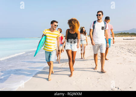Group of friends walking on the beach, carrying surfboards Stock Photo