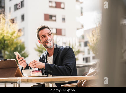 Businessman sitting in cafe, drinking coffee, using smartphone Stock Photo