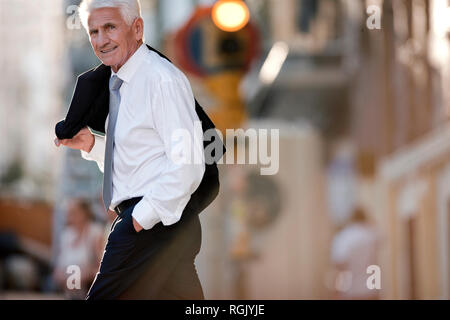 Mature businessman carrying his jacket over one shoulder smiles he poses for a portrait while crossing a city street. Stock Photo