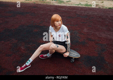 Cool young woman sitting on carver skateboard outdoors Stock Photo