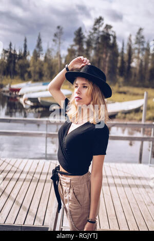 Sweden, Lapland, portrait of fashionable blond woman wearing black hat standing on jetty Stock Photo