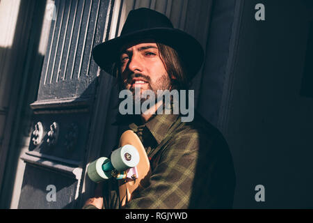 USA, New York City, portrait of bearded man with skateboard and black hat leaning at house entrance Stock Photo