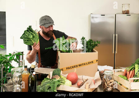 Mature man with delivery service packing organic vegetables in cardboard Stock Photo