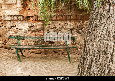 Old grunge wooden broken bench on decayed abandoned brick rural wall background in small neglected country village Stock Photo