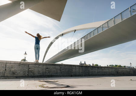 Netherlands, Maastricht, young woman standing on a wall at a bridge Stock Photo