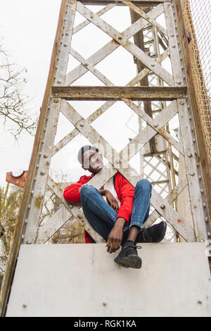 Young man sitting on pillar, smiling Stock Photo