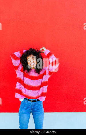 Portrait of laughing young woman with curly hair standing in front of red wall Stock Photo