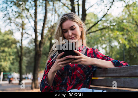 Young woman sitting on bench outdoors using mini tablet Stock Photo
