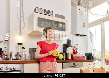 Smiling woman having a coffee break in kitchen Stock Photo
