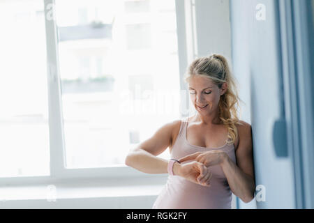 Smiling pregnant woman standing at the window looking at smartwatch Stock Photo