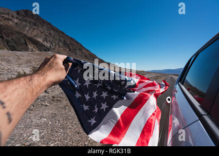 USA, California, Death Valley, man's hand holding American flag besides car Stock Photo