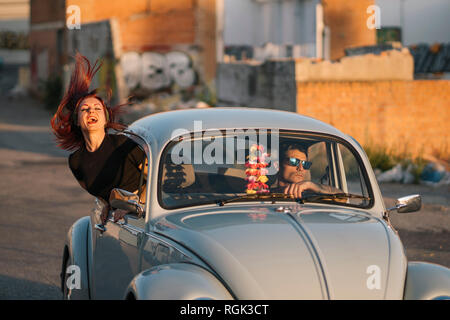 Couple driving in a vintage car, woman banding out of window Stock Photo