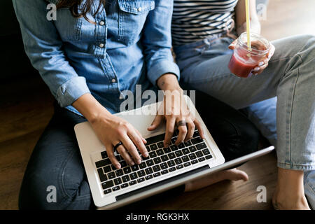 Close-up of two young women sitting on floor with soft drink and laptop Stock Photo