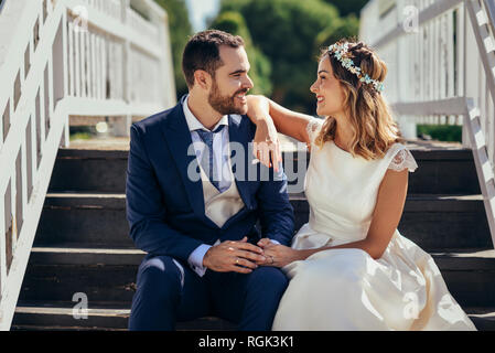 Happy bridal couple sitting on stairs holding hands Stock Photo