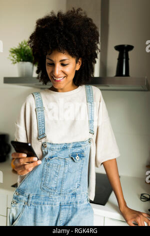 Smiling woman using cell phone in kitchen at home Stock Photo